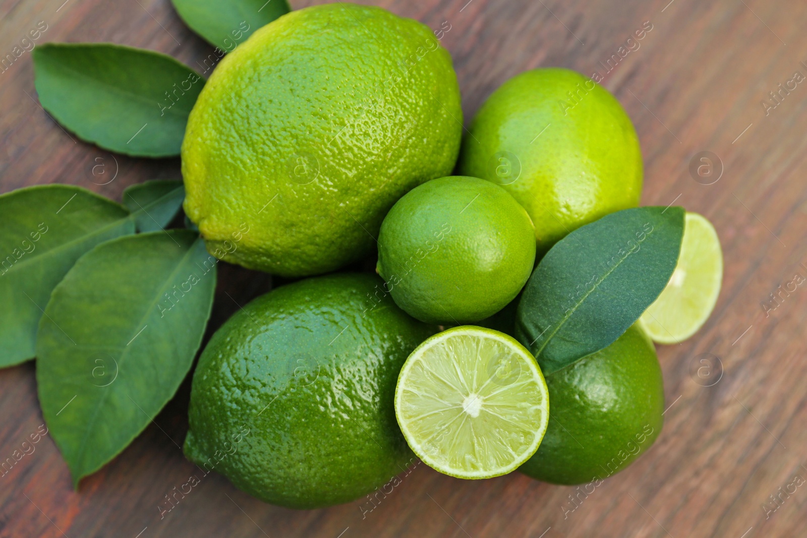 Photo of Whole and cut fresh ripe limes with green leaf on wooden table, flat lay