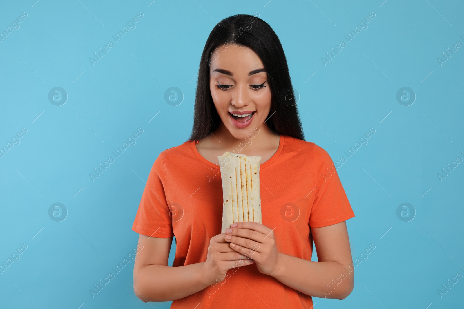 Photo of Young woman eating tasty shawarma on turquoise background