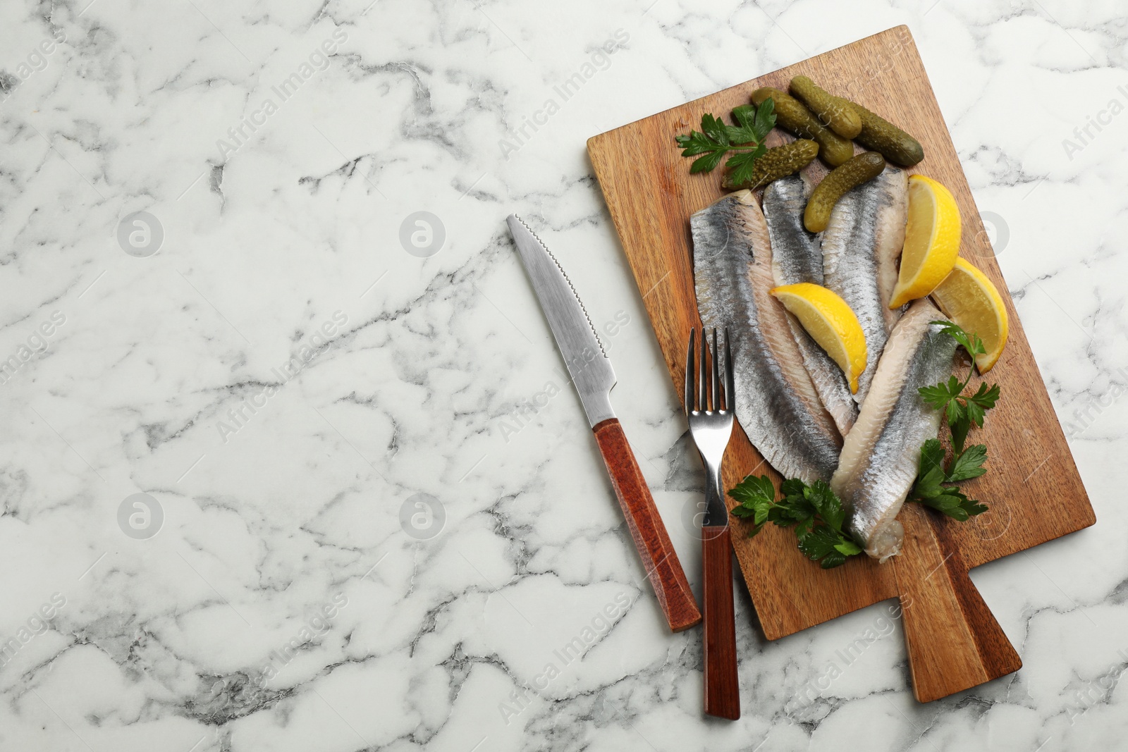 Photo of Salted herring fillets served with pickles, parsley and lemon on white marble table, flat lay. Space for text