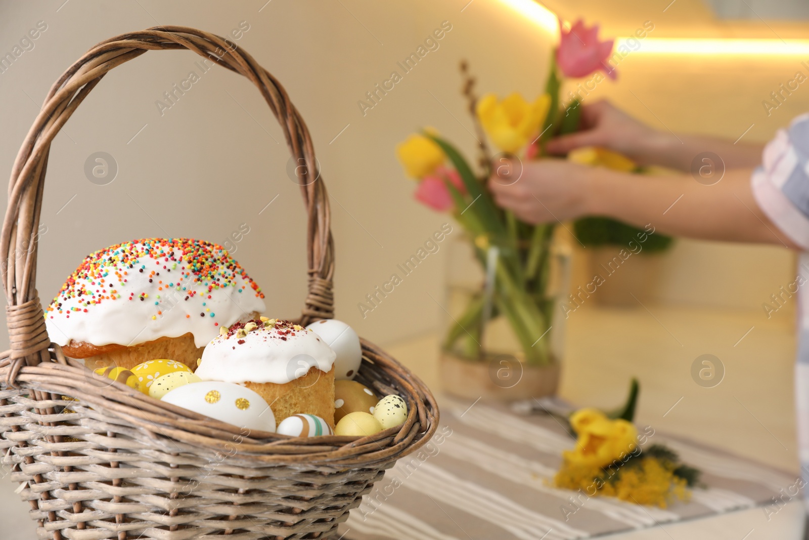 Photo of Basket with traditional Easter cakes and dyed eggs on table indoors, space for text