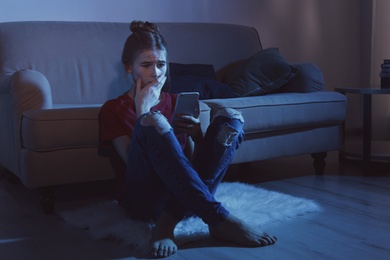 Photo of Terrified teenage girl with smartphone in dark room. Danger of internet