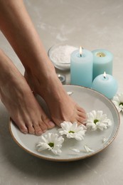 Photo of Woman soaking her feet in bowl with water and flowers on grey marble floor, closeup. Pedicure procedure