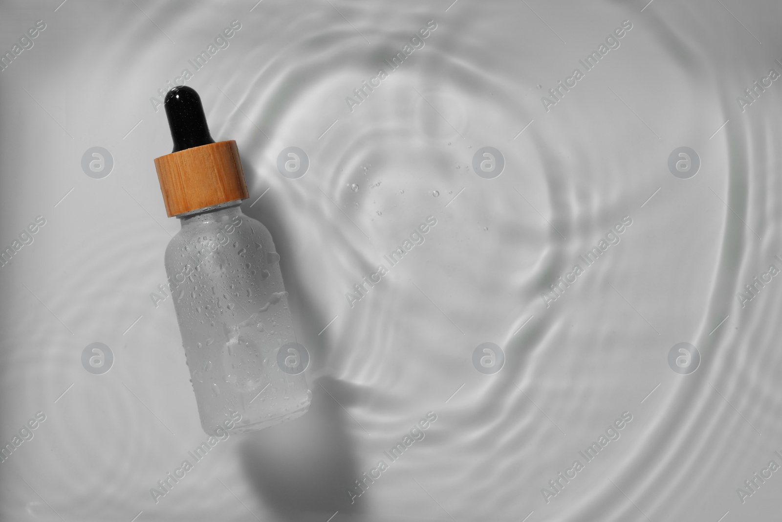 Photo of Bottle of cosmetic product in water on white background, top view. Space for text