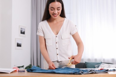 Photo of Happy woman making ripped jeans at table indoors