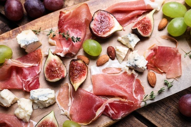 Photo of Ripe figs and prosciutto served on wooden table, above view