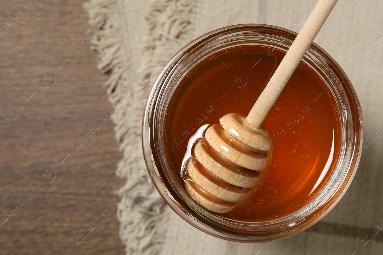 Photo of Dipper with honey in jar on wooden table, top view. Space for text