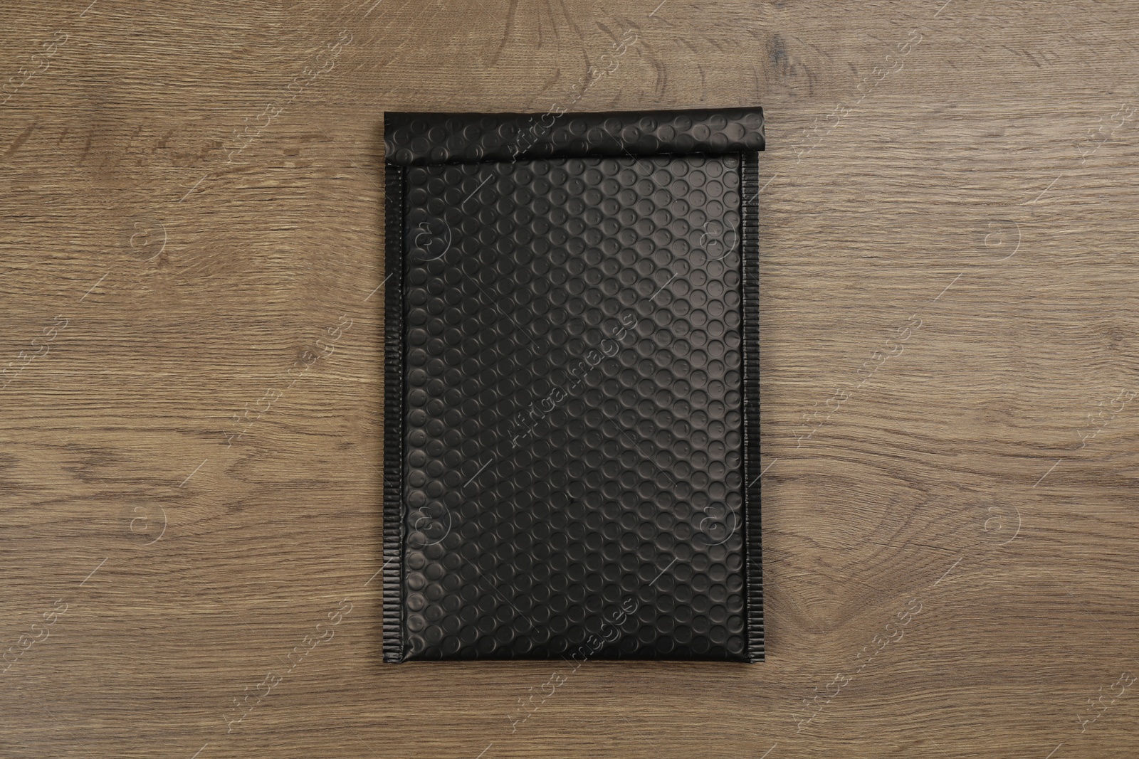 Photo of Black padded envelope with bubble wrap on wooden background, top view