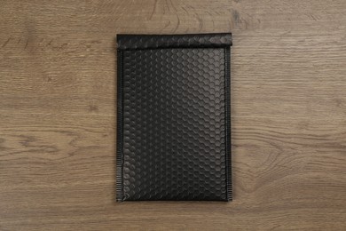 Photo of Black padded envelope with bubble wrap on wooden background, top view