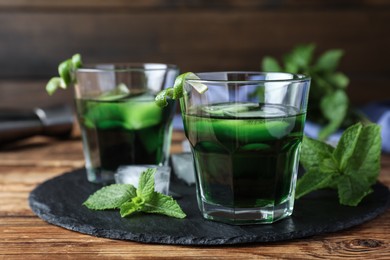 Photo of Delicious mint liqueur with green leaves on wooden table