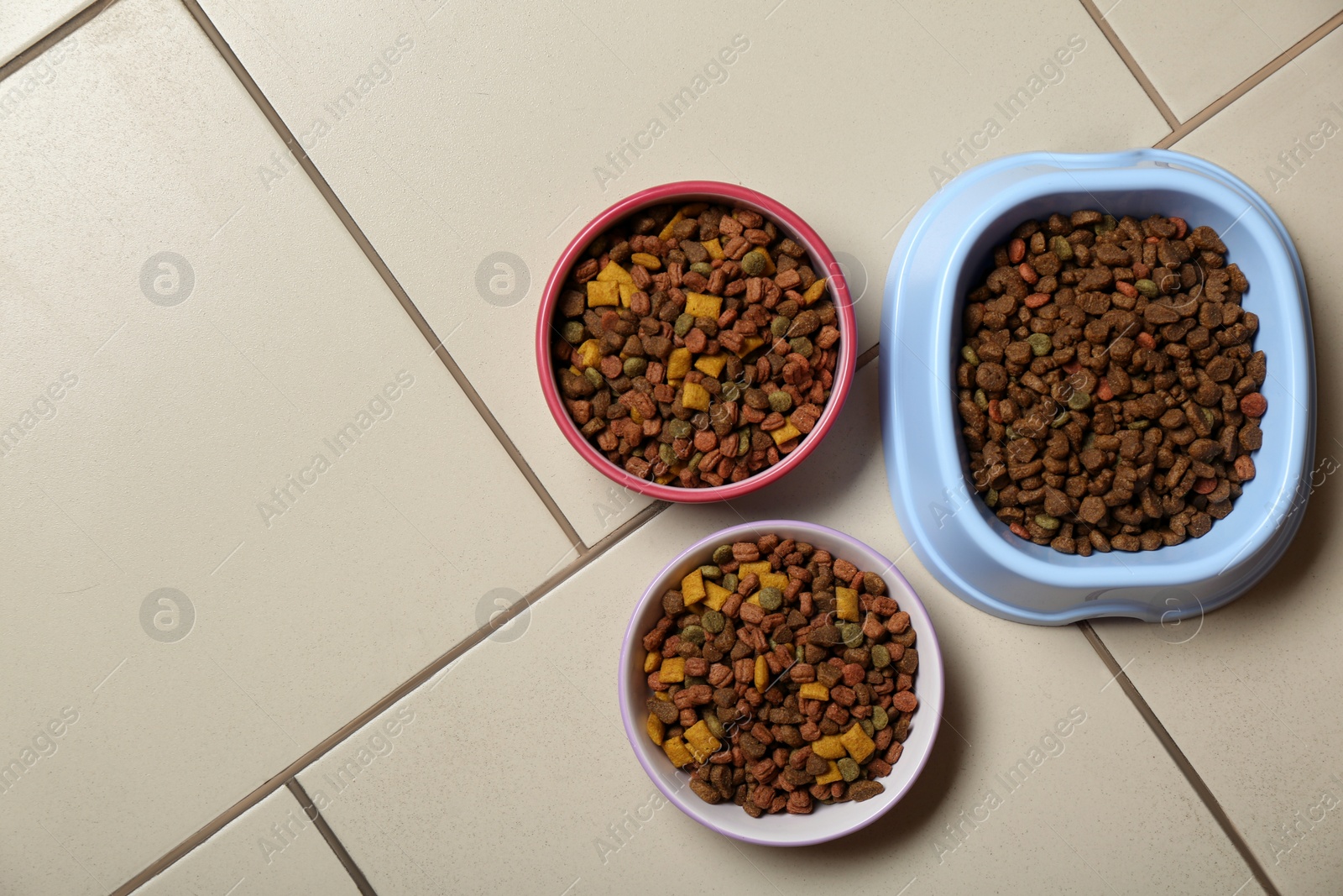 Photo of Pet bowls with dry food on floor, flat lay. Space for text