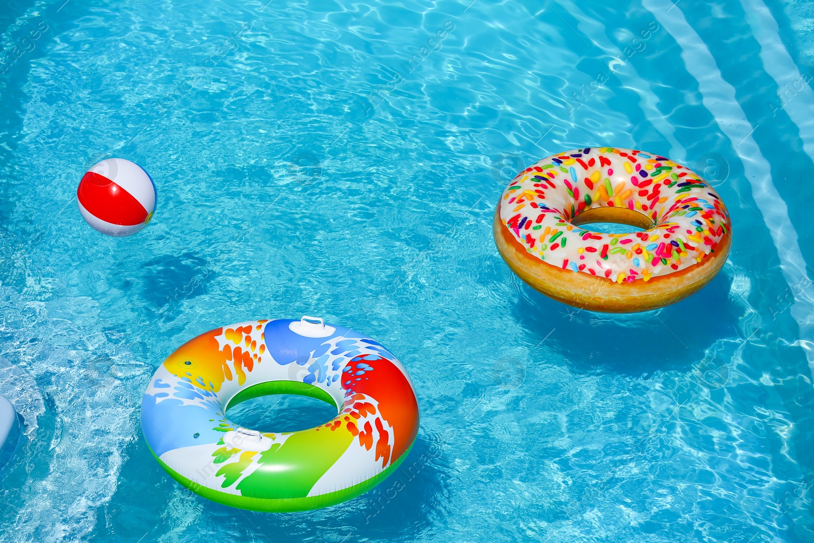 Photo of Bright inflatable rings and beach ball floating in swimming pool on sunny day