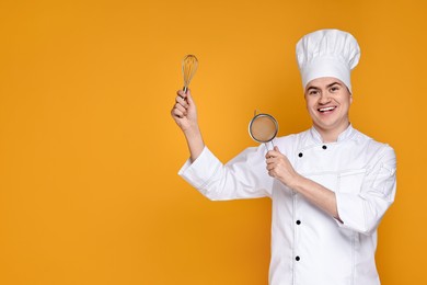 Portrait of happy confectioner in uniform holding whisk and sieve on orange background, space for text