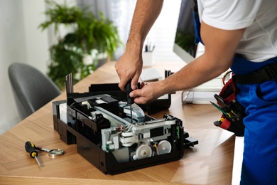 Repairman with screwdriver fixing modern printer indoors, closeup