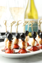 Tasty canapes with black olives, mozzarella and cherry tomatoes on white marble table, closeup