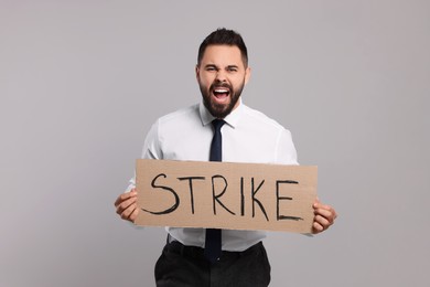 Photo of Angry young man holding cardboard banner with word Strike on light grey background