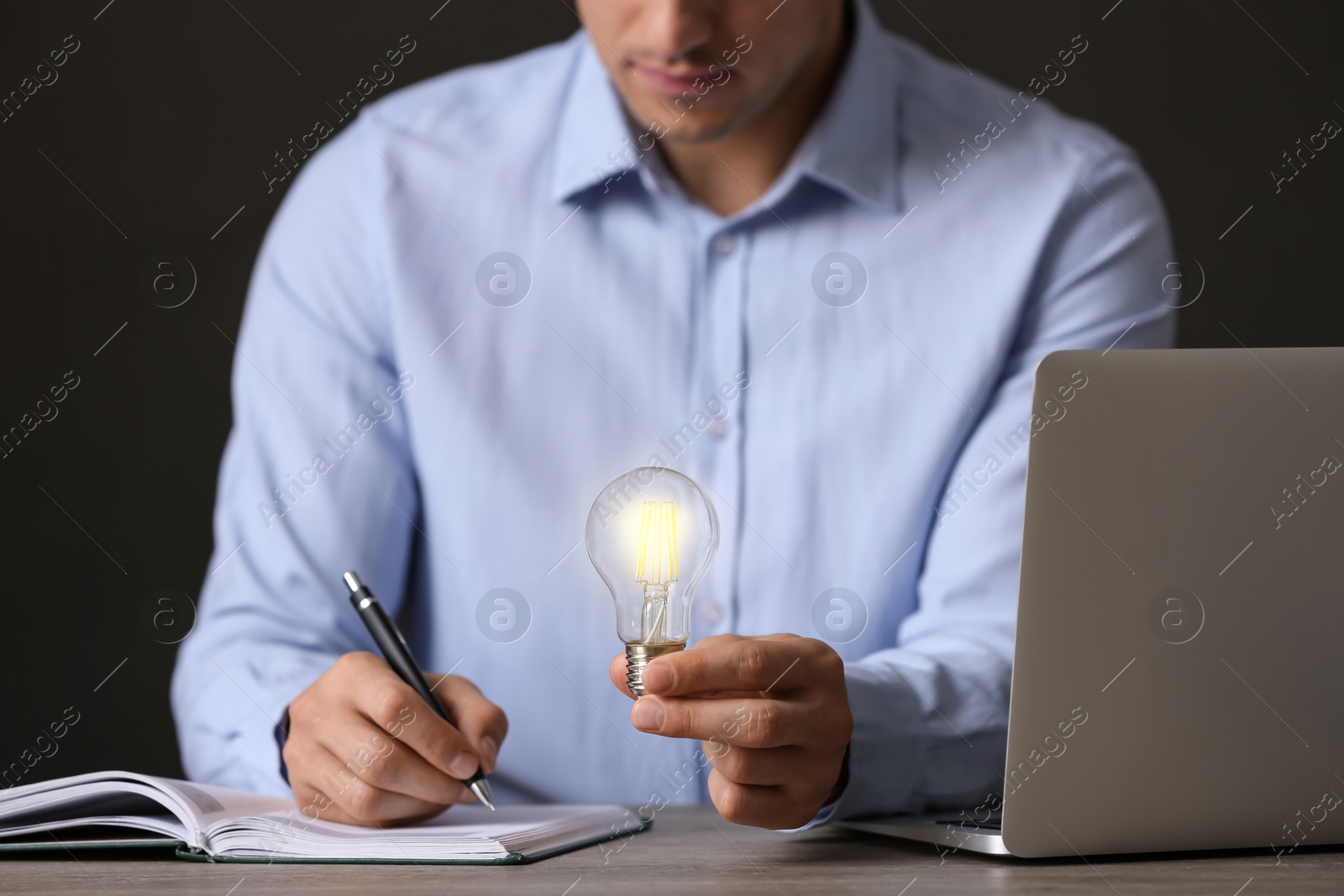 Photo of Glow up your ideas. Closeup view of man holding light bulb while working at wooden desk