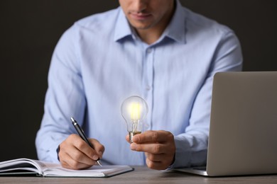 Glow up your ideas. Closeup view of man holding light bulb while working at wooden desk