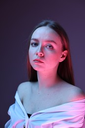 Photo of Fashionable portrait of beautiful young woman on purple background in neon lights