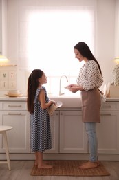 Photo of Mother and daughter wiping dishes together in kitchen