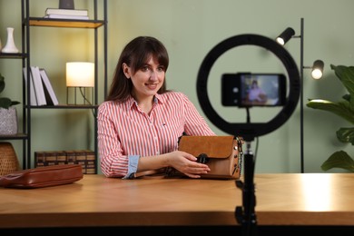 Photo of Smiling fashion blogger recording video while showing bag at home