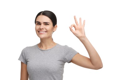 Photo of Young woman with clean teeth smiling and showing ok gesture on white background