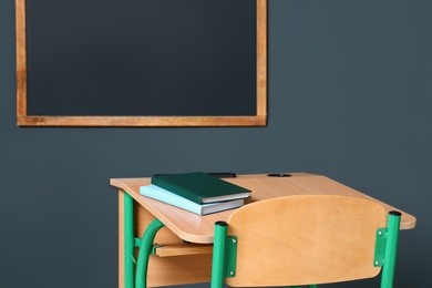 Photo of Wooden school desk with stationery near blackboard on grey wall