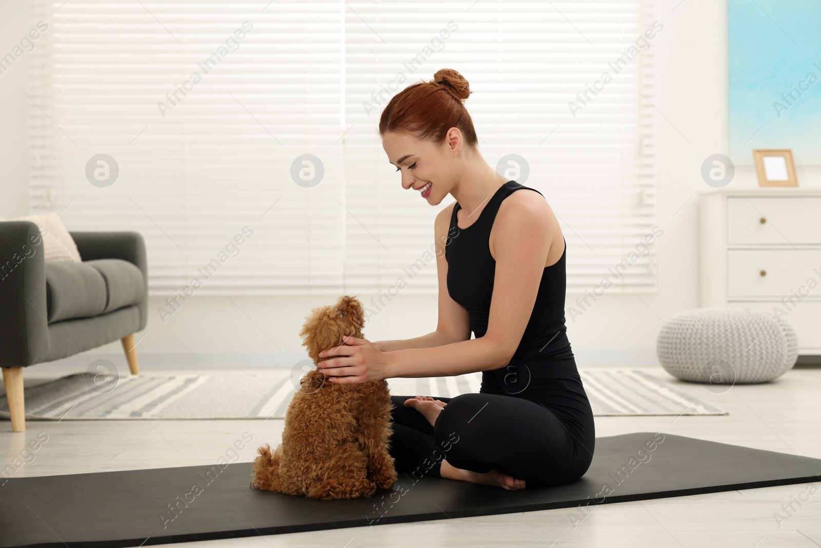 Photo of Happy young woman practicing yoga on mat with her cute dog at home