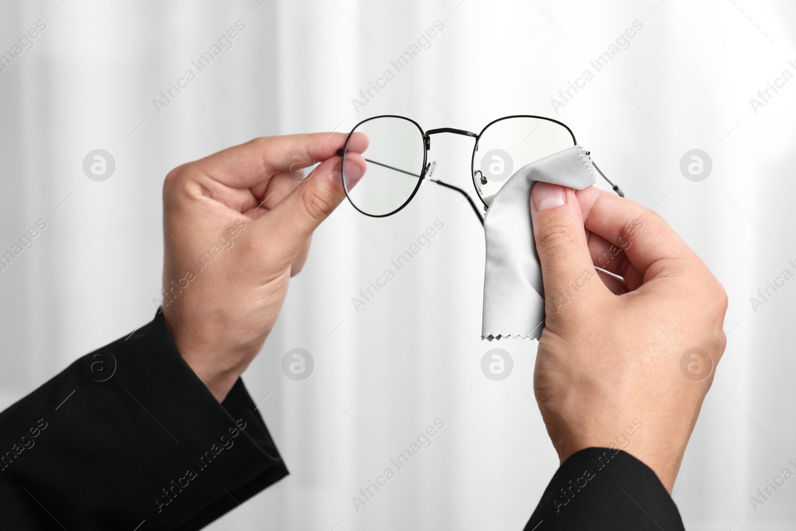 Photo of Man wiping glasses with microfiber cloth indoors, closeup