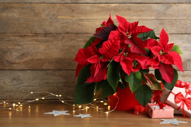 Photo of Poinsettia (traditional Christmas flower), string lights and gift boxes on wooden table. Space for text