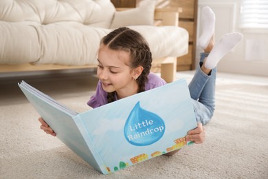 Photo of Cute little girl reading book on floor at home