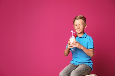 Photo of Little boy with glass of milk shake on stool against color background