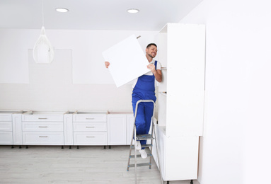 Worker installing door of cabinet in kitchen