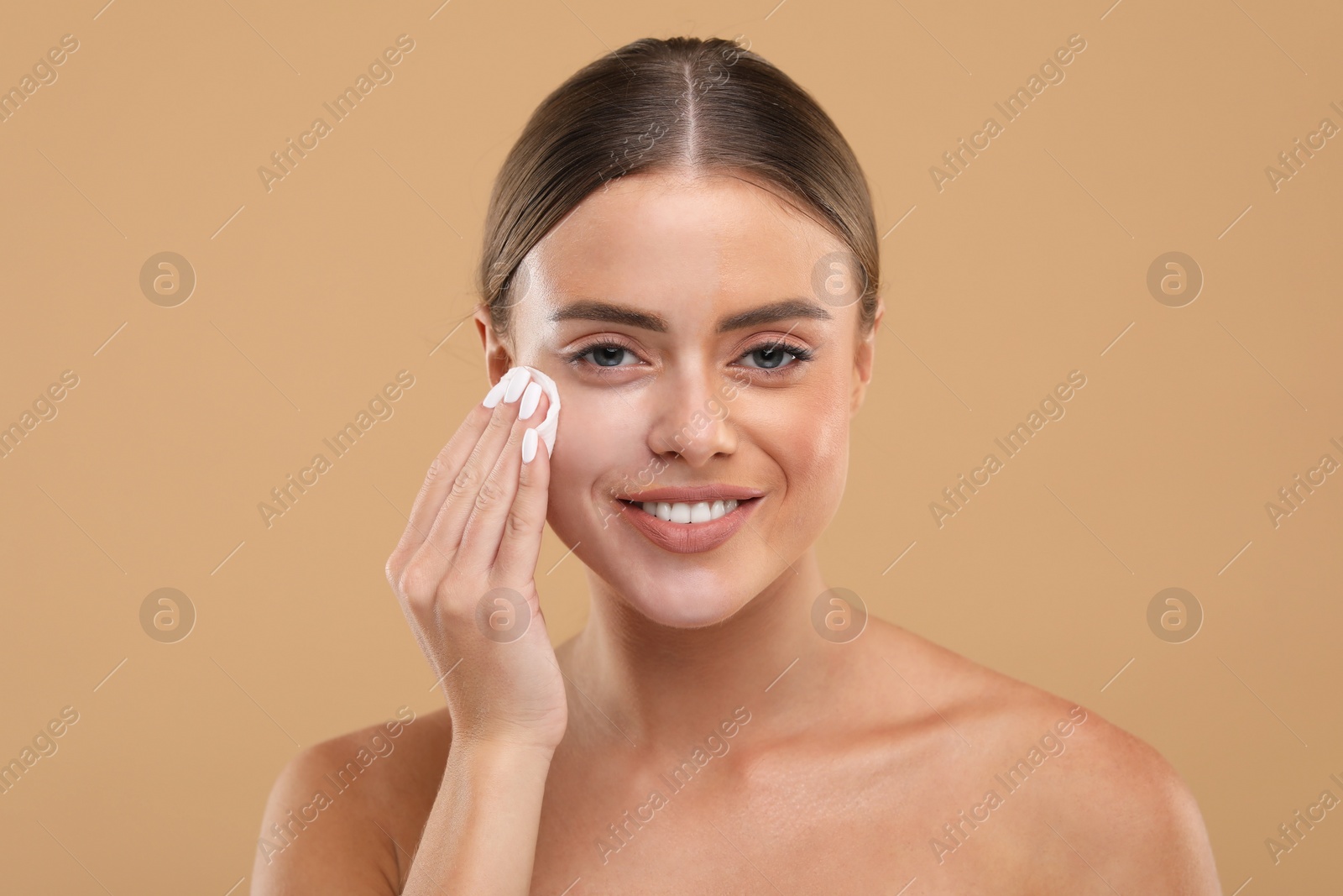 Photo of Beautiful woman removing makeup with cotton pad on beige background