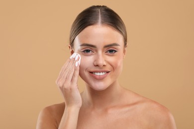 Beautiful woman removing makeup with cotton pad on beige background