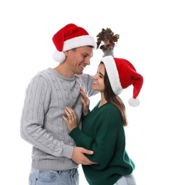 Photo of Happy couple in Santa hats standing under mistletoe wreath on white background