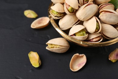 Tasty pistachios in bowl on black table, closeup. Space for text