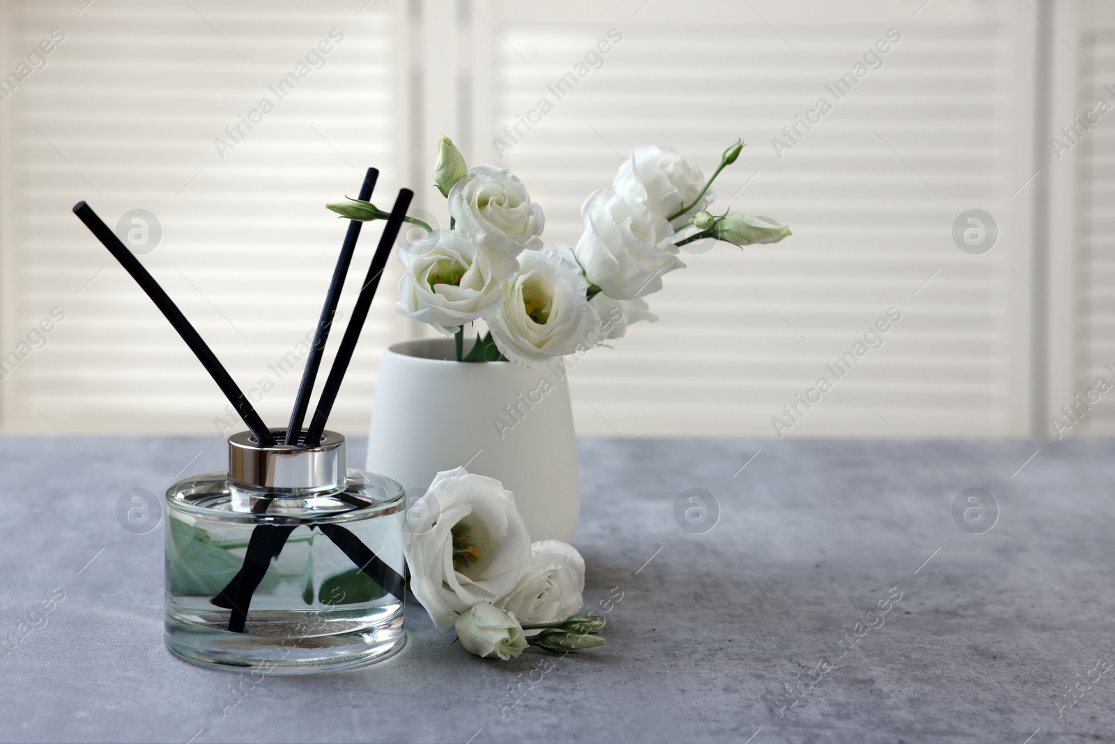 Photo of Reed diffuser and vase with eustoma flowers on gray marble table, space for text