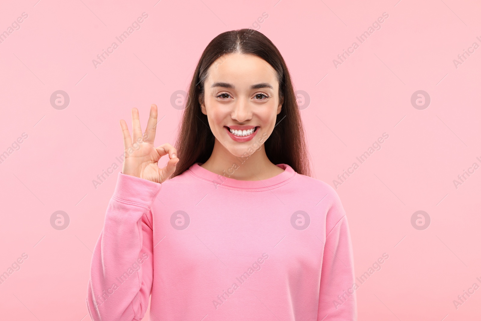 Photo of Beautiful woman with clean teeth showing OK gesture on pink background