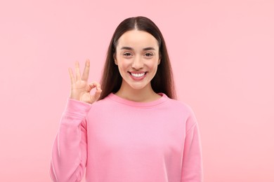 Beautiful woman with clean teeth showing OK gesture on pink background