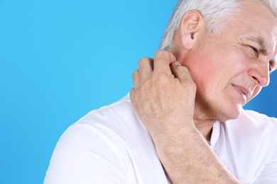 Senior man scratching neck on color background, closeup with space for text. Allergy symptom