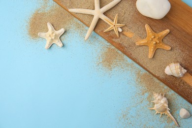 Photo of Wooden plank with beautiful starfishes, sea shells, stones and sand on light blue background, flat lay. Space for text