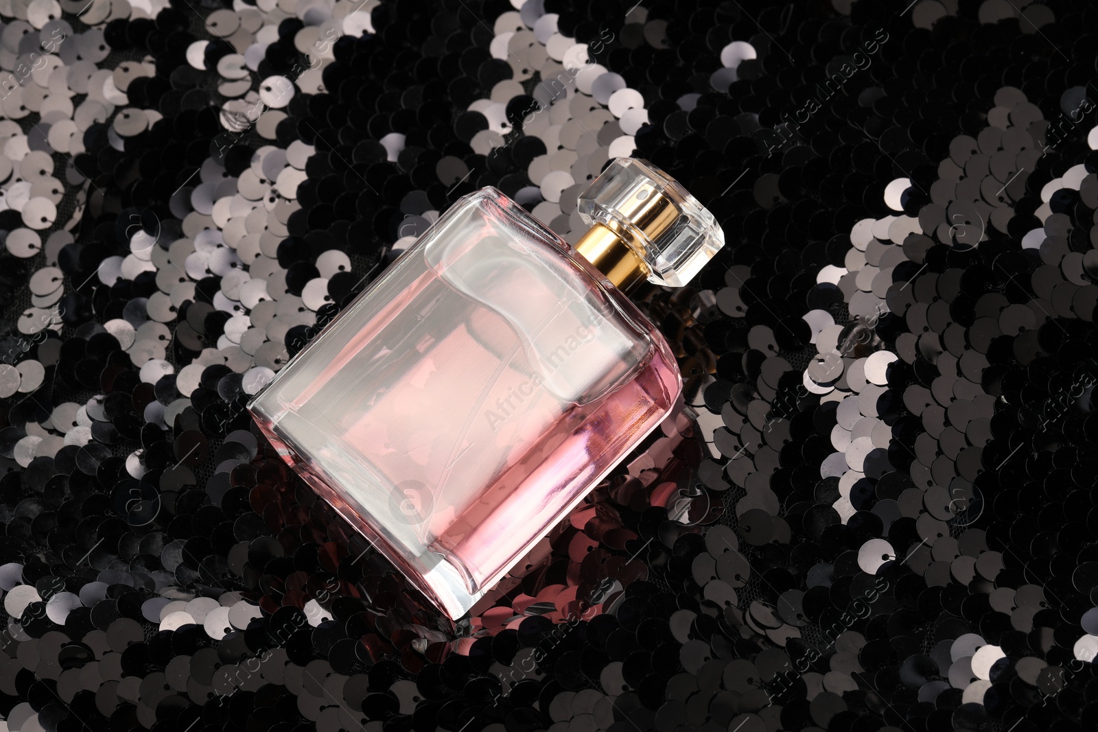 Photo of Luxury perfume in bottle on fabric with shiny sequins