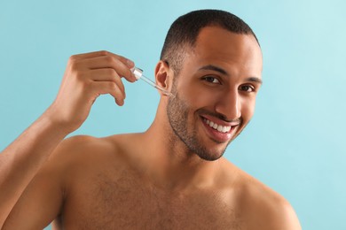 Photo of Handsome man applying cosmetic serum onto face on light blue background