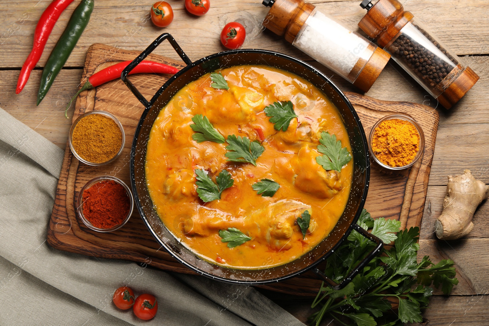 Photo of Tasty chicken curry with parsley and ingredients on wooden table, flat lay