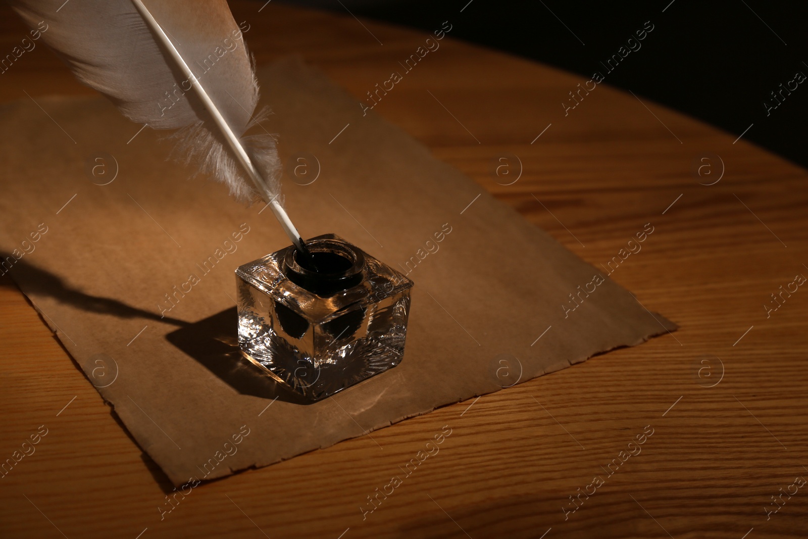 Photo of Feather pen, inkwell and blank parchment on table in darkness. Space for text