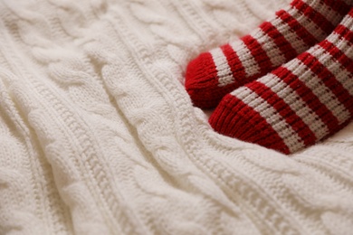 Photo of Woman in warm socks on knitted blanket, closeup. Space for text