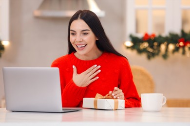 Celebrating Christmas online with exchanged by mail presents. Smiling woman thanking for gift during video call at home