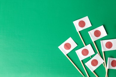 Photo of Small paper flags of Japan on green background, flat lay. Space for text