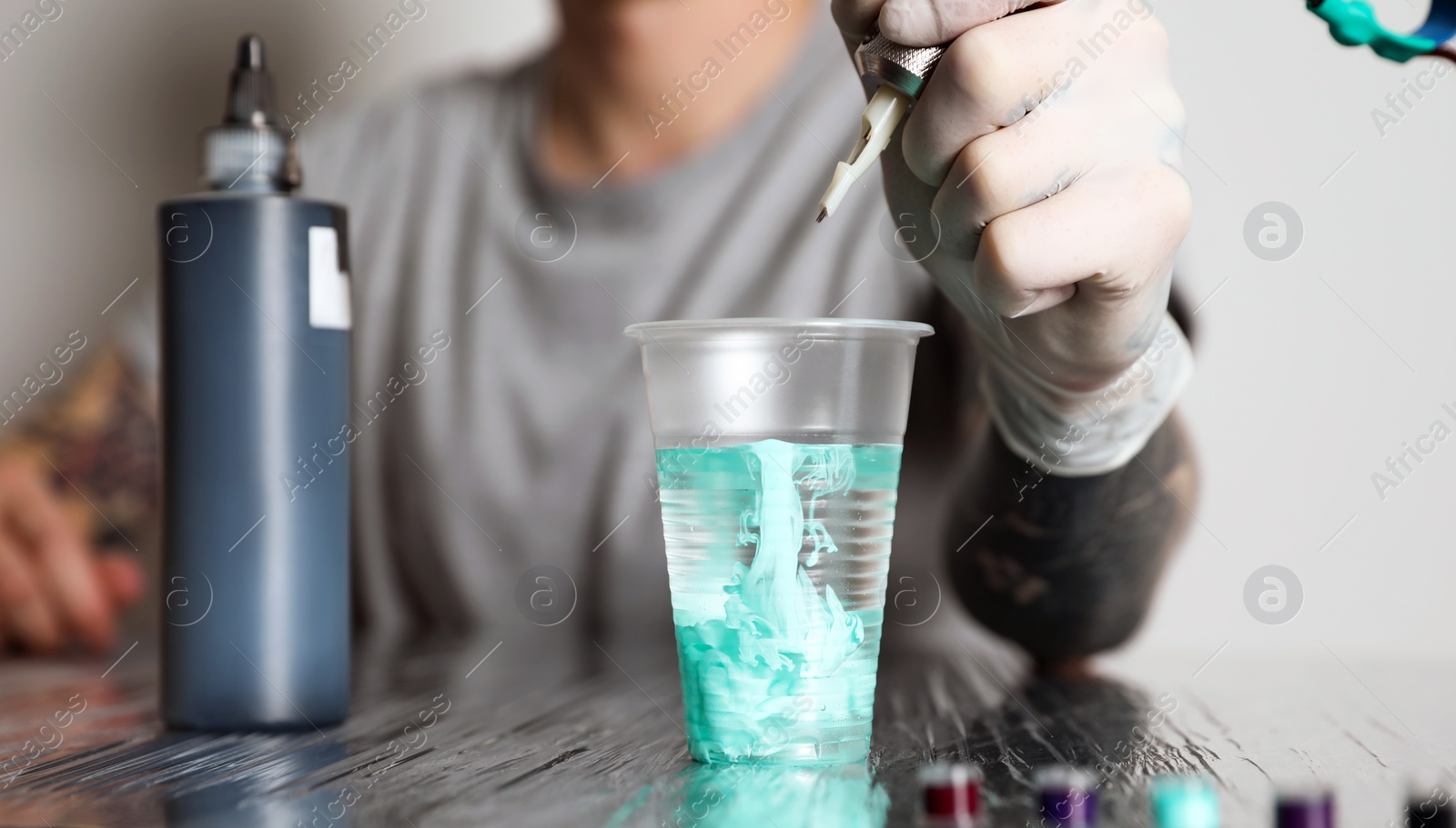 Photo of Tattoo artist cleaning machine needle at table, closeup