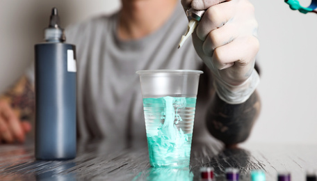 Photo of Tattoo artist cleaning machine needle at table, closeup